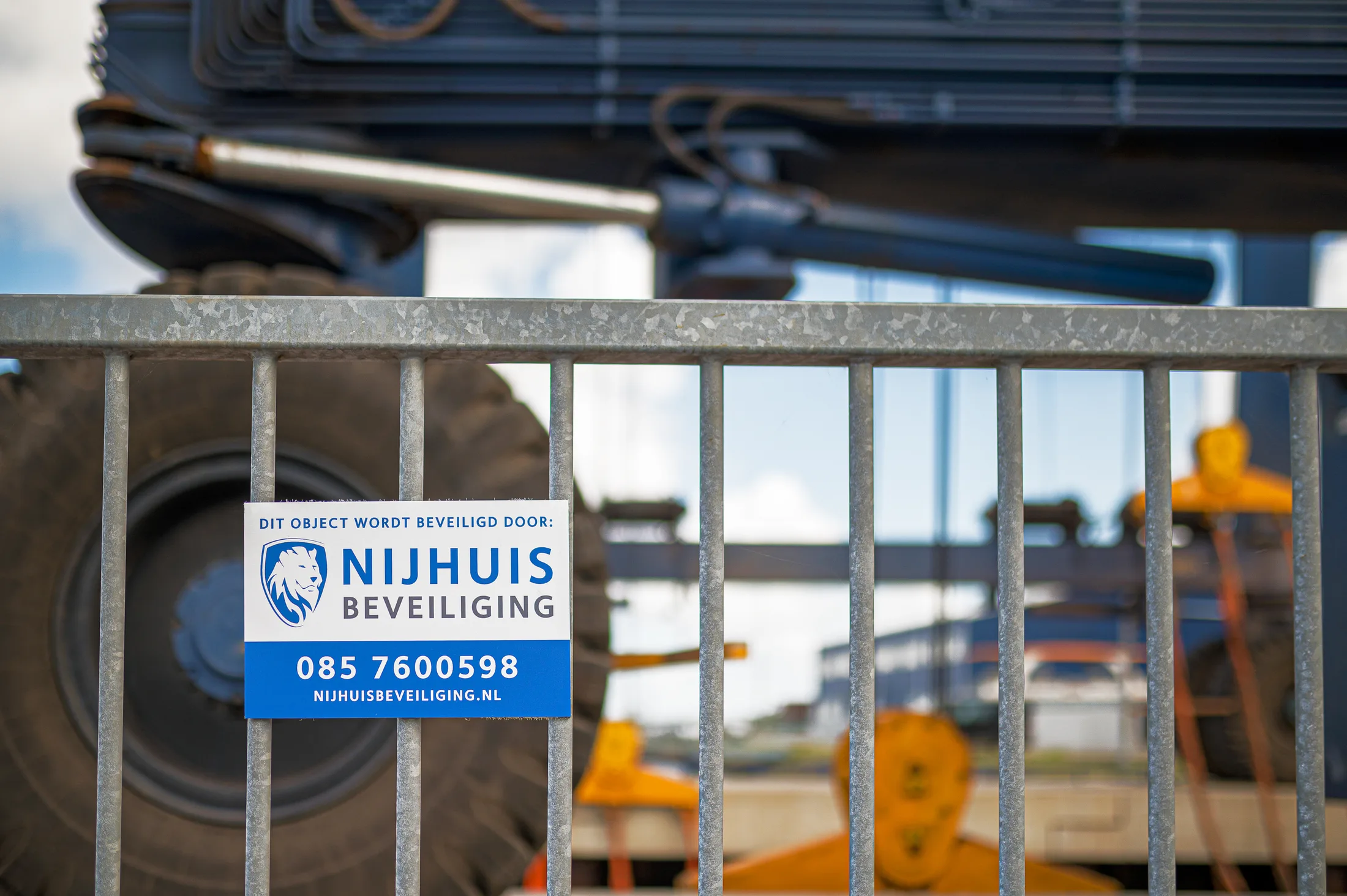 Bord van Nijhuis Beveiliging aan een hek met materieel erachter